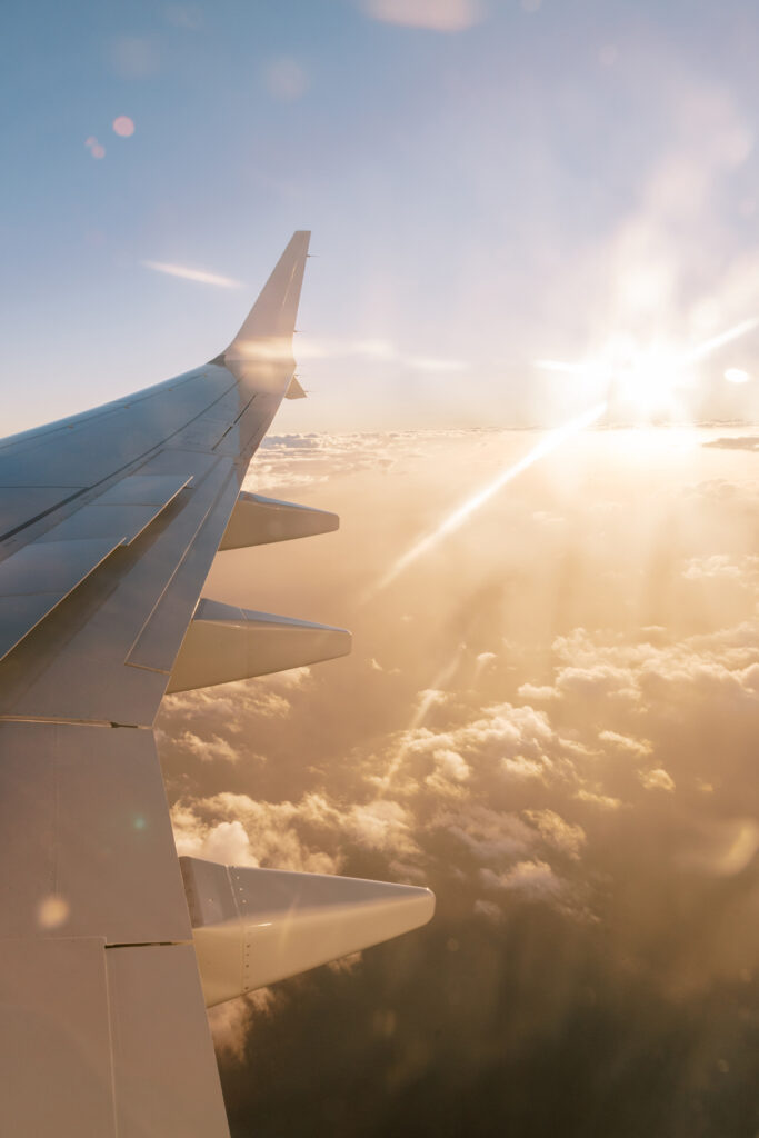Photo of plane wing in the sky, with clouds and sunshine rays.
